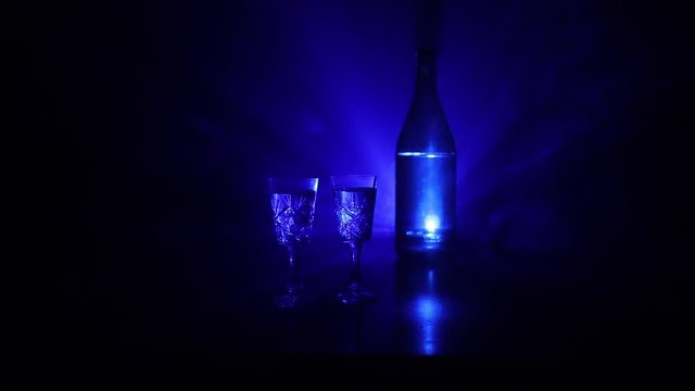 Two glasses of Vodka with bottle on dark foggy club style background with glowing lights (Laser, Stobe) Multi colored. Club drinks theme decoration. Empty space. Selective focus
