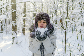Fototapeta na wymiar A woman holds a handful of snow in her hands and blows on it. Winter in the forest. The sun sparkles.