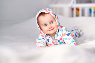 Cute smiling baby in a stylish hoodie lying on a white blanket on parents bed