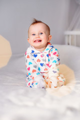 Cute smiling baby in a stylish hoodie sitting on a white blanket on parents bed. Child laughing.