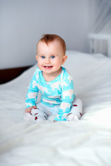 Cute smiling baby sitting on the white blanket at the bed