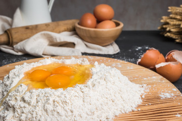 Eggs, dough, flour and rolling-pin on wooden table background. Preparation for making homemade ravioli pasta