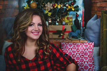 close-up portrait of a very cute and beautiful smiling girl in a shirt on a christmas tree background and a window