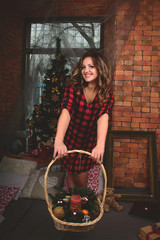 portrait of a beautiful girl in a shirt with a basket on the background of a Christmas tree.  A basket with candles and sprigs of spruce with cones.
