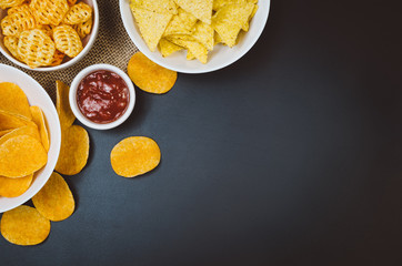 Party snacks - potato chips and snacks in bowl on black slate table. Photograph taken from above,...