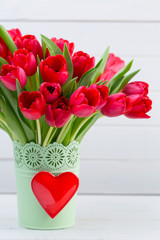 Fresh red tulip flowers bouquet on shelf in front of wooden wall.