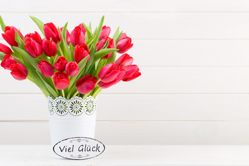Fresh red tulip flowers bouquet on shelf in front of wooden wall.