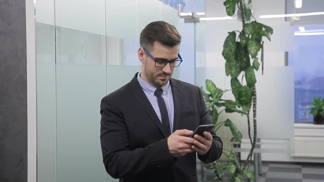 Male businessman reads mobile phone before a speech in front of media. Portrait of young man in a strict suit to prepare for an interest and pre-checks the news on a computer technology device.