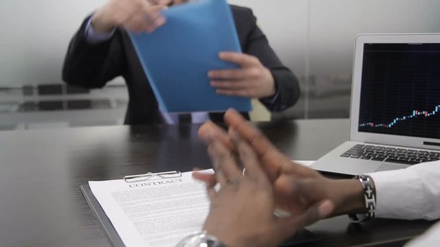 Successful businessmen enters into contract in modern office. Two men are communicating at table in large company. Confident male talk actively, discussing terms of mutually beneficial agreement and