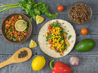 Tortilla cooking Mexican Taco, vegetarian salad, parsley, avocado and spices on a dark wooden table.