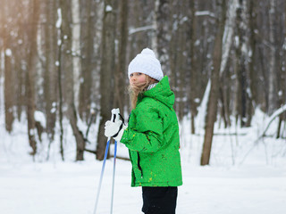 Fototapeta na wymiar The girl in the green jacket in the sun in the winter woods on skis.