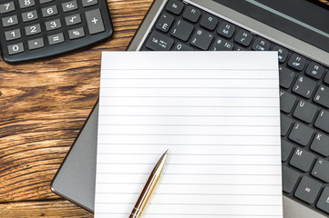 Notepad with pen on the laptop keyboard and calculator on desk. Top view.