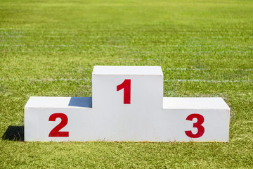 White wooden winner podium placed on green grass sport field on a sunny day