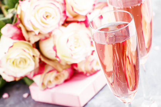 Bouquet of white and red roses, gift box, glasses with pink champagne for a pair of lovers for St. Valentines Day, gray background, selective focus