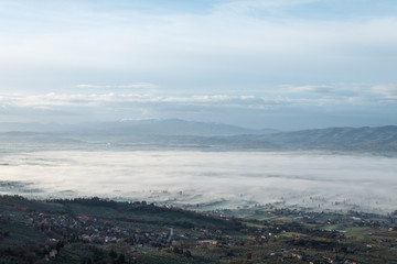 Beautiful view of Umbria valley in a winter morning, with fog covering trees and houses