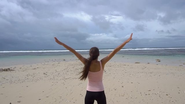 Woman in sports wear rise hands on beach