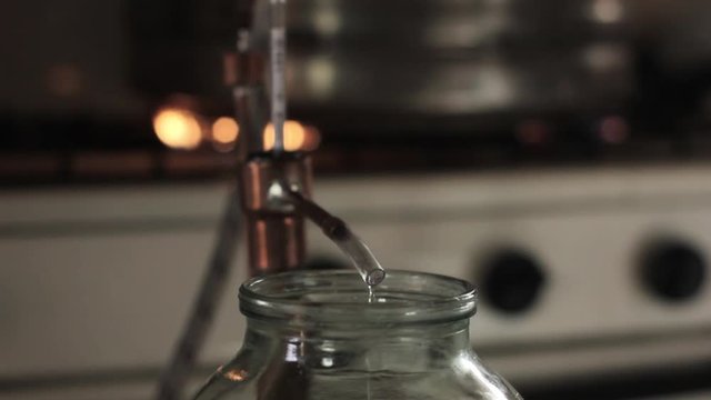 Home production of alcohol on flame fire. Alcohol distillation equipment, hooch fluid flow into glass jar