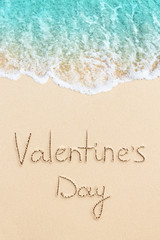Valentine's Day handwritten on the sand of beach with ocean wave