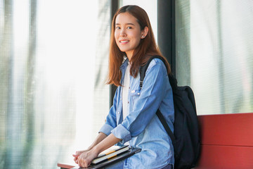 Portrait of asian female colleges student holding textbook in her hands and standing outdoors at university campus