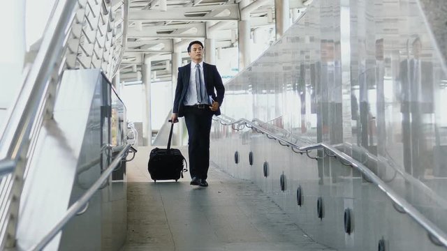 Asian young businessman walking dragging luggage with hastiness