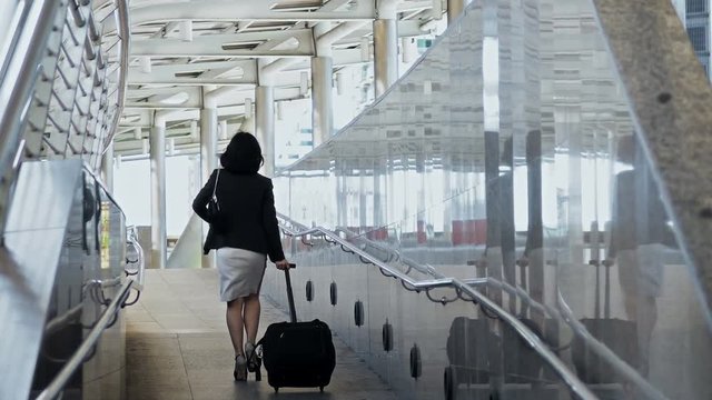 Young businesswoman walking dragging luggage with hastiness