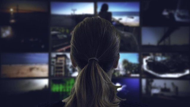 Watching TV Television Screens. Head shot of a ponytail woman watching many videos in a wall of televisions