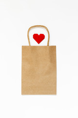 Craft paper bag and red origami heart on white background. Mockup. Concept of shopping.