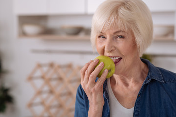 Cheerful elderly woman eating an apple