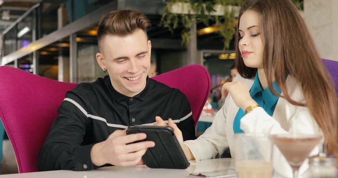Stylish young couple talking in cafe, looking together at tablet PC