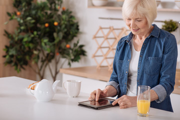 Cheerful aged woman using her tablet in the kitchen