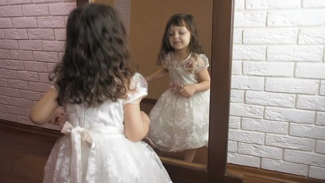 A little girl by the mirror. A girl in a beautiful dress by the mirror.