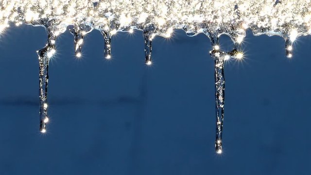 The icicle is glitter in the sun, a close up. Water drops falls from an icicle with a stars reflection of the sun. Sparkle of icicle.