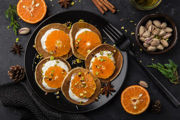 delicious pancakes with clementines, cream and pistachios on black plate