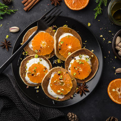 delicious pancakes with clementines, cream and pistachios on black plate