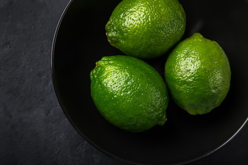 close up of fresh green lime in black bowl, dark background