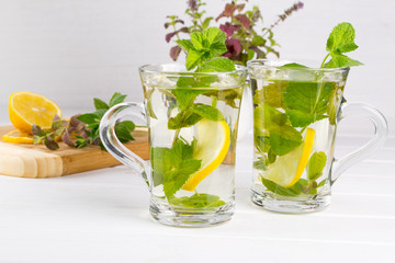 Two glass cups fresh mint tea with lemon and a bunch of mint in vase