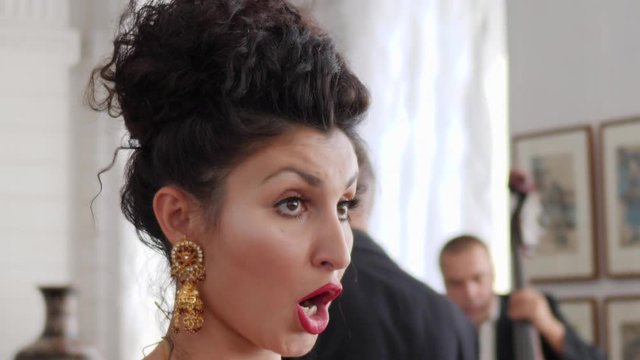 portrait of an attractive girl with beautiful earrings and red lips emotionally sings into a microphone on scene closeup