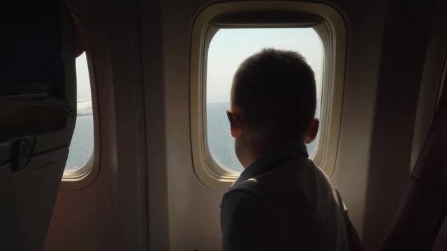 Boy looking out the illuminator how plane flying over the sea and coming in for landing
