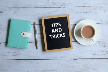 Top view of notebook,pen,a cup of coffee, and blackboard written with 'TIPS AND TRICKS' on white...