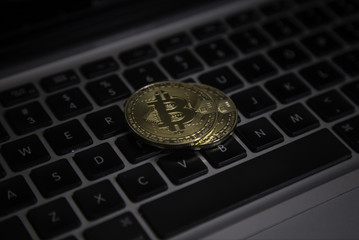 A horizontal close up image of a golden coin of Bitcoin on keyboard of a laptop. Bitcoin is a crypto currency and a worldwide payment system.