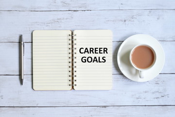 Top view of a cup of coffee,pen and notebook written with 'CAREER GOALS' on white wooden background.