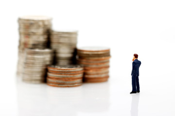 Miniature people: Businessman standing  with looking and thinking to stack of coins how to increase revenue. Concept of Money, Financial, Business Growth concept.