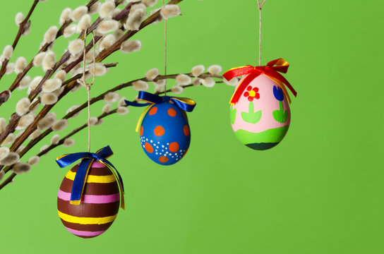 Three colored easter eggs on willow bouquet with pussy willows. Religious decoration. Paschal eggs on branches with furry catkins in vase. Salix. Front view, horizontal, on green background. Photo.