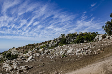 The mountainside is strewn with stones and in the background incredibly beautiful clouds in the sky