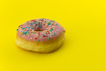 Close-up of a pink glazed donut isolated on yellow background. Strong candy contrast.