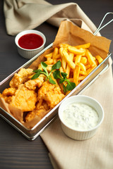 chicken nuggets with french fries and different sauces on wooden board,