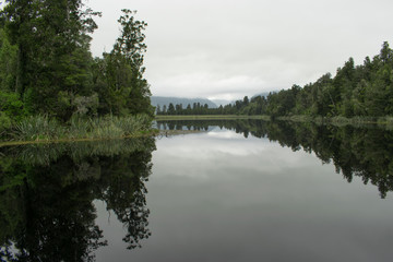 Reflection of trees in the water at Lake Matheson on an overcast day,