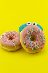 Close-up with many multicolored glazed donuts on yellow background.