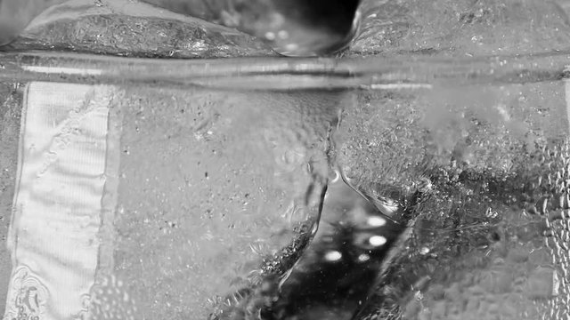 Macro shot of ice cubes being dropped into a glass of water against a black background