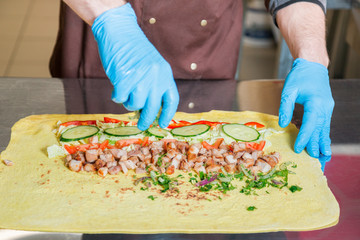 Cook prepares a shawarma. Ingredients on a big pita bread.